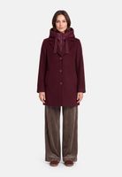 Frau trägt burgunderfarbenen Hooded-Cape-Mantel mit Knopfleiste, graue Velourhose und braune Flats.
