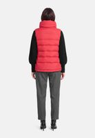 Person von hinten in rotem Puffervest, schwarzem Shirt, grauen Hosen und schwarzen Pumps.