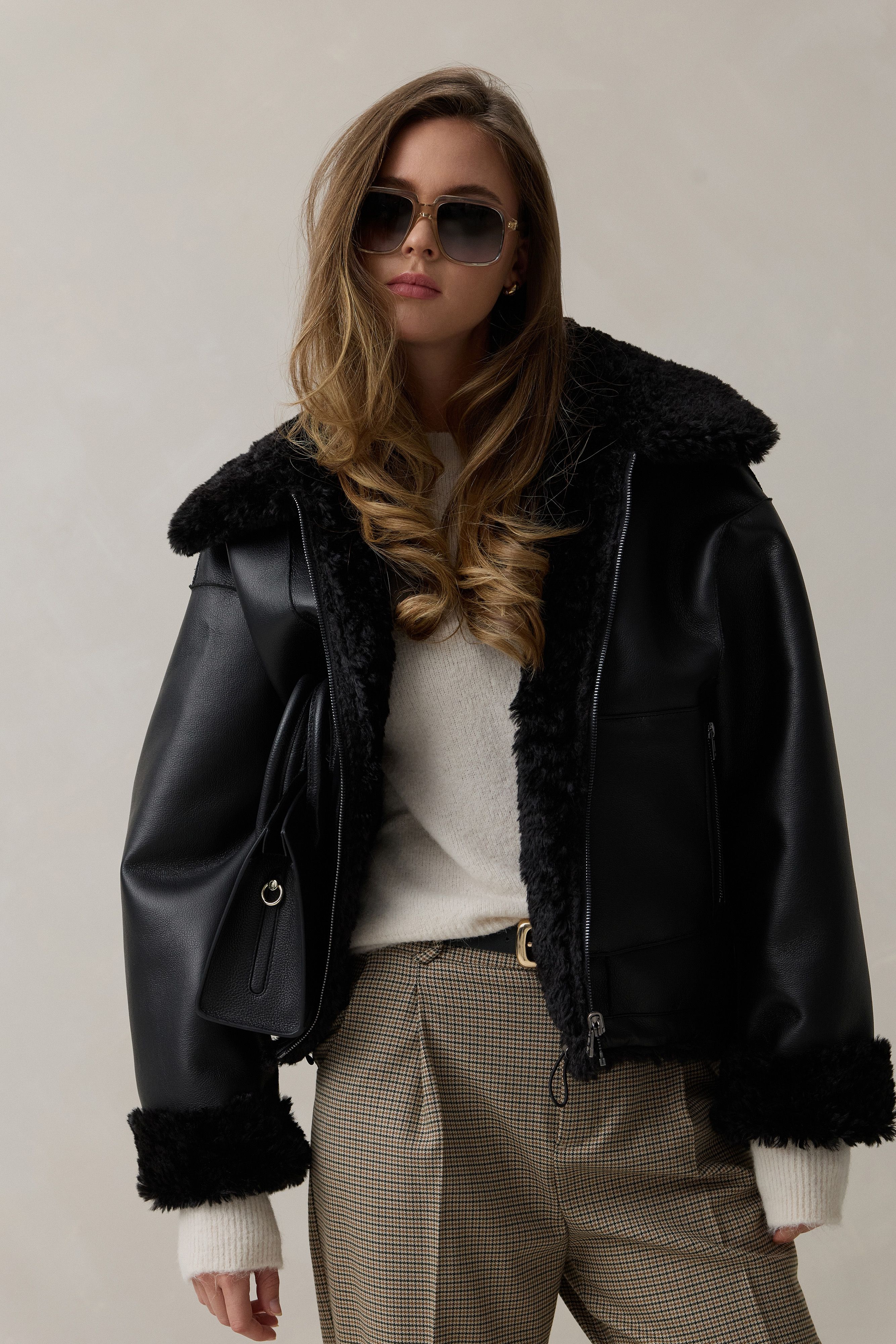 Frau mit schwarzem Lederjacken mit Fellkragen, Sonnenbrille und hüttigen Hosen, lässiger Look.