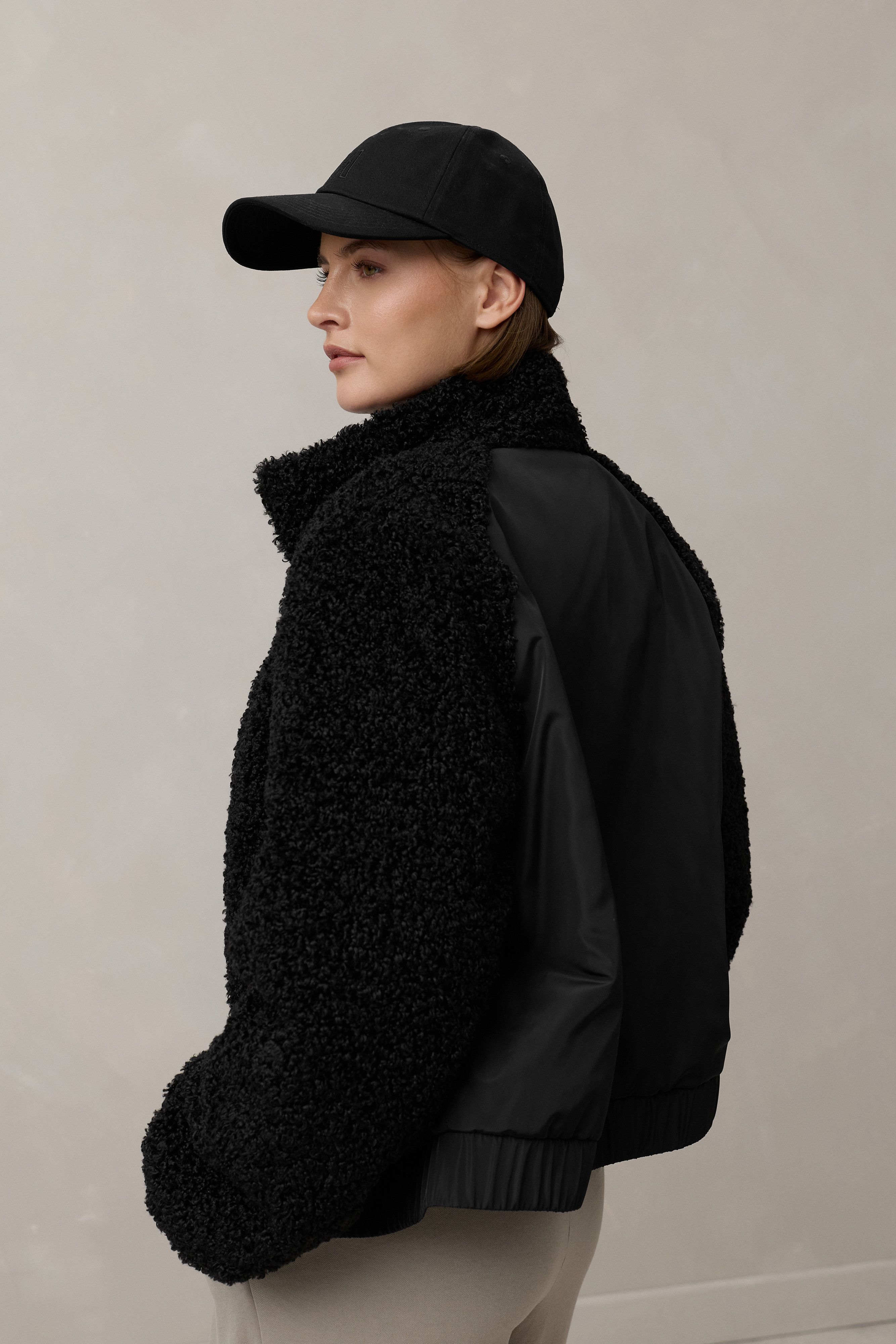 Frau trägt schwarzen oversized-Bomberjacken mit Futter und Basecap, beige Hose.