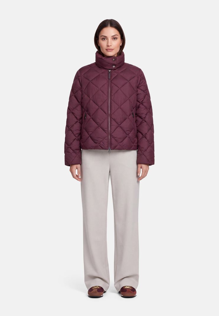 Frau trägt burgunderfarbenen Quilted-Jacket mit hellgrauen Hosen und flachen Schuhen.