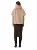 Elegante Frau mit beigeem oversized Mantel, braunem Wickelrock und schwarzen Stiefeln von hinten.