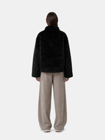 Person trägt oversized schwarzen Strickmantel mit beige Pantalons, von hinten gesehen.