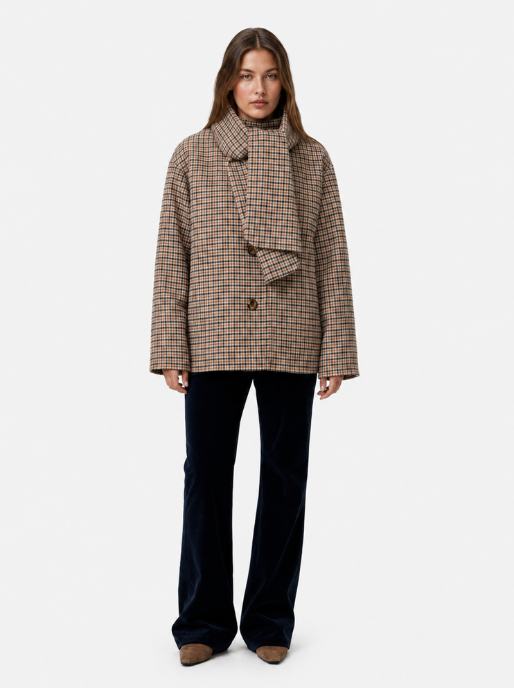 Frau trägt hellbraunen karierten Blazer mit Knopfdetails und dunkelblauen weiten Hosen, beige Schuhe.